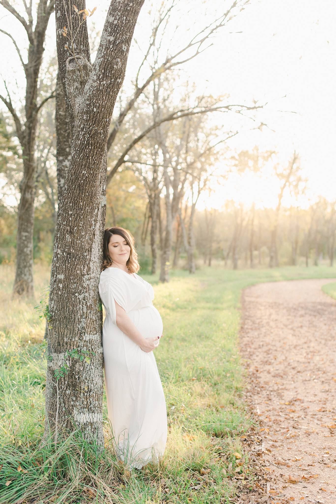 mom holding her belly leaning on a tree